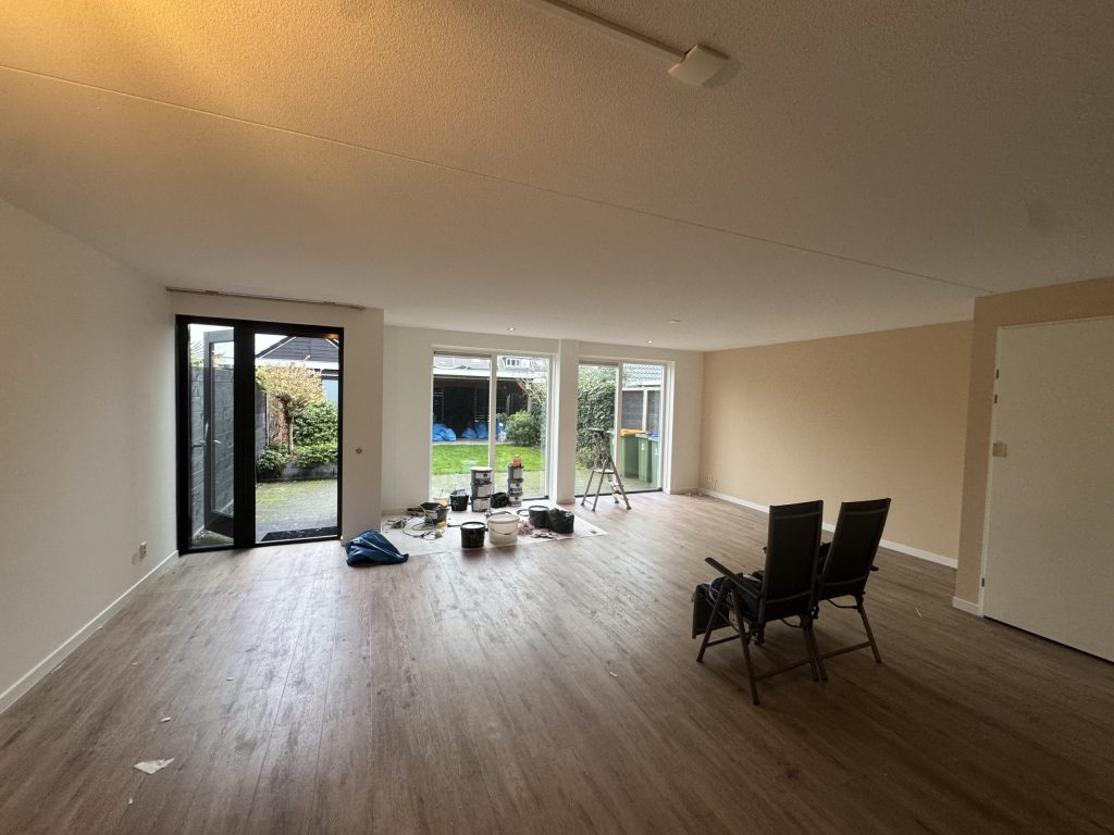 Woonkamer van een rijtjeshuis met lichte wanden en tuindeuren, tijdens het afwerken