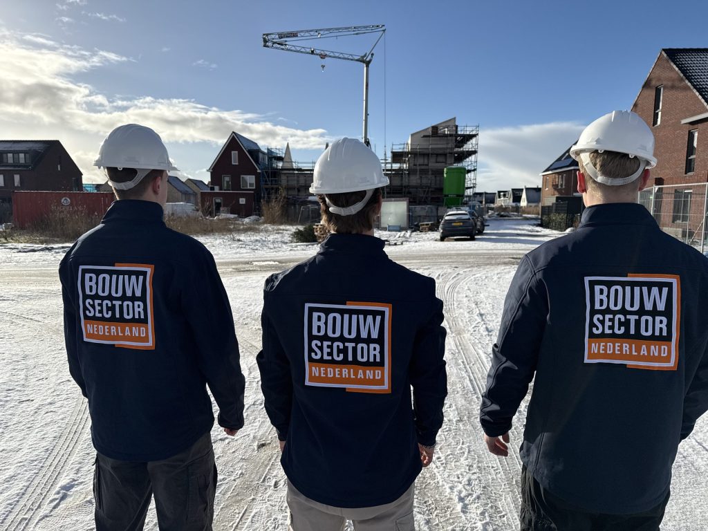 Drie vakmensen van Bouwsector Nederland met witte helm en bedrijfsjas op een besneeuwde bouwplaats
